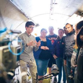 Dr. 扎克·梅塞尔和学生们在爱德华兹加速器实验室的飞行时间隧道里, located on campus.